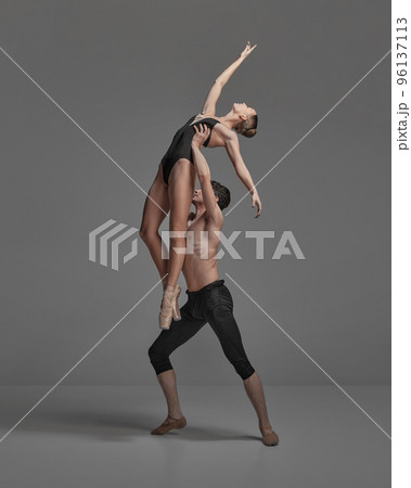 Young man and woman, ballet dancers performing isolated over dark grey studio background. Growing high Young man and woman, ballet dancers performing isolated over dark grey studio background. Growing high 96137113