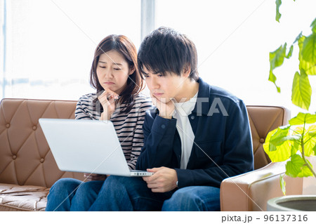 カップル夫婦-リビングのソファに座りパソコン作業で困る男女2人 96137316