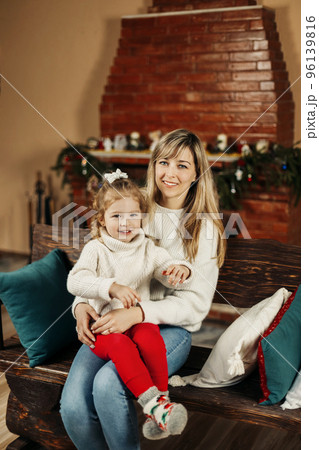 Happy mom and baby daughter reading having fun by the fireplace on Christmas or New Year's Eve. Parenthood, childhood, time together, holidays Happy mom and baby daughter reading having fun by the fireplace on Christmas or New Year's Eve. Parenthood, childhood, time together, holidays 96139816