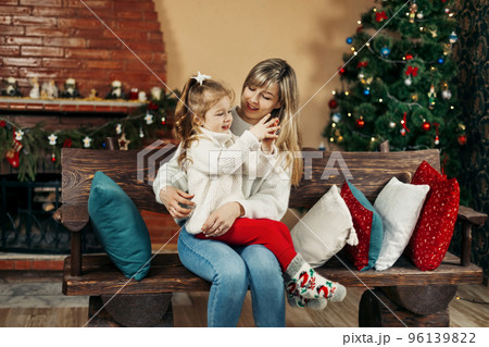 Mom and daughter in casual clothes play and hug against the background of a Christmas tree. Christmas and New Year, Christmas holidays, Christmas time. Childhood, motherhood, time together Mom and daughter in casual clothes play and hug against the background of a Christmas tree. Christmas and New Year, Christmas holidays, Christmas time. Childhood, motherhood, time together 96139822