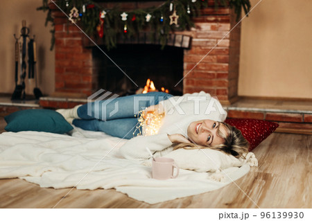 A charming young woman lies on a rug by the fireplace on Christmas Eve A charming young woman lies on a rug by the fireplace on Christmas Eve 96139930