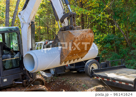 An excavation worker uses tractor to lift concrete sewage pipes from trucks placed on ground to prepare for underground installation 96141624