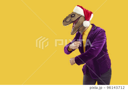 Funny man in dinosaur mask, Christmas hat and party suit dancing on copy space background Funny man in dinosaur mask, Christmas hat and party suit dancing on copy space background 96143712