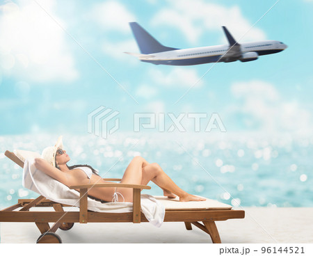 Beautiful girl sitting on a deck chair at the beach at sunset with airplane on background 96144521