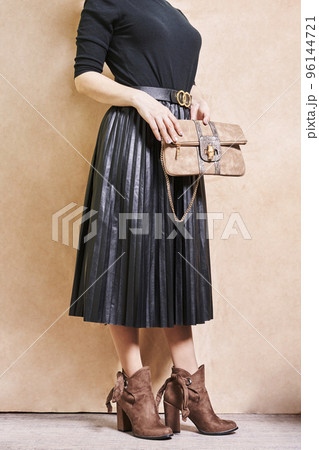 a woman wearing a skirt and holding a handbag in her right hand, standing against a beige wall background 96144721
