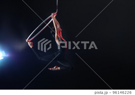 Young woman performing acrobatic element on aerial ring against dark background. Space for text 96146226