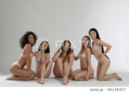 Group of women with different body types in jeans and underwear taking selfie against light 96146457