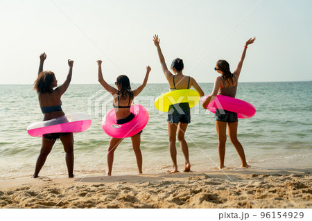 Back of teeage girls with pink and yellow swimming ring look at the sea and enjoy with dancing Back of teeage girls with pink and yellow swimming ring look at the sea and enjoy with dancing 96154929