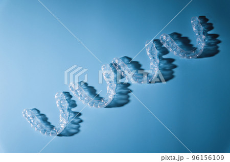 background for dental clinic or orthodontics. invisible plastic new braces lie in a row on a blue background, studio shot with shadows background for dental clinic or orthodontics. invisible plastic new braces lie in a row on a blue background, studio shot with shadows 96156109
