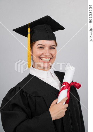 Smiling woman in graduation gown holding diploma on white background. Vertical photo. Smiling woman in graduation gown holding diploma on white background. Vertical photo. 96158554