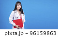 Cheerful asian woman doctor wear uniform with stethoscope holding clipboard over isolated blue 96159863