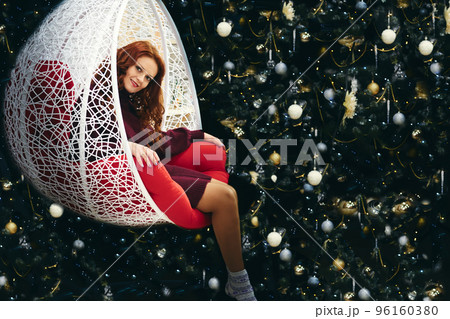 Young pretty woman in a wicker rocking chair near the New Year tree Young pretty woman in a wicker rocking chair near the New Year tree 96160380