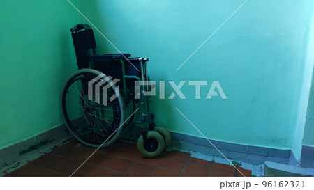 Folding wheelchair, standing folded against a green wall in the corner 96162321