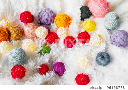 Bright multicolored knitting yarn and a luminous garland in the form of balls lie on fluffy blanket. Bright multicolored knitting yarn and a luminous garland in the form of balls lie on fluffy blanket. 96168778
