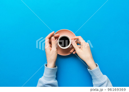 Minimalistic style woman hand holding a cup of coffee on Colored background. Flat lay, top view cappuccino cup. Empty place for text, copy space. Coffee addiction. Top view, flat lay Minimalistic style woman hand holding a cup of coffee on Colored background. Flat lay, top view cappuccino cup. Empty place for text, copy space. Coffee addiction. Top view, flat lay 96169369