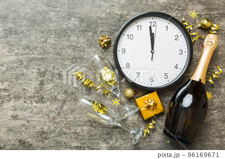 New year celebration concept with a bottle of champagne and two glasses toasting. Christmas gift box, alarm clock and fir tree branch on colored table. Top view Copy space New year celebration concept with a bottle of champagne and two glasses toasting. Christmas gift box, alarm clock and fir tree branch on colored table. Top view Copy space 96169671