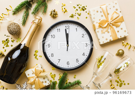 New year celebration concept with a bottle of champagne and two glasses toasting. Christmas gift box, alarm clock and fir tree branch on colored table. Top view Copy space New year celebration concept with a bottle of champagne and two glasses toasting. Christmas gift box, alarm clock and fir tree branch on colored table. Top view Copy space 96169673
