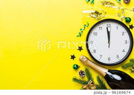 New year celebration concept with a bottle of champagne and two glasses toasting. Christmas gift box, alarm clock and fir tree branch on colored table. Top view Copy space New year celebration concept with a bottle of champagne and two glasses toasting. Christmas gift box, alarm clock and fir tree branch on colored table. Top view Copy space 96169674