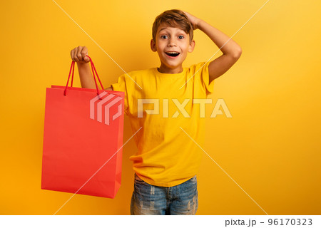 Happy child are amazed about a shop sales. surprised, expression. Yellow background color Happy child are amazed about a shop sales. surprised, expression. Yellow background color 96170323