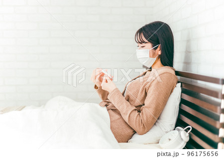 ベッドで体温計を使って体温を測る発熱したマスク姿の日本人女性 ベッドで体温計を使って体温を測る発熱したマスク姿の日本人女性 96175656