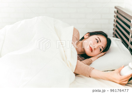 ベッドで眠くて寝ぼけながら目覚まし時計を止める低血圧の日本人女性 96176477