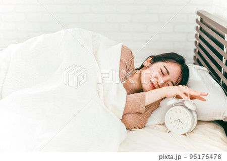 ベッドで眠くて寝ぼけながら目覚まし時計を止める低血圧の日本人女性 96176478