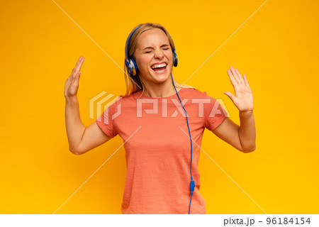 Blonde girl listens to music with headset. Joyful expression on yellow background 96184154