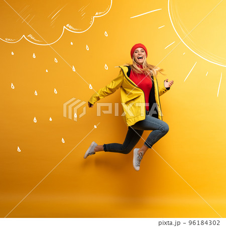 Girl with jacket jumps to the sun from the rainy weather. Joyful expression. Yellow background Girl with jacket jumps to the sun from the rainy weather. Joyful expression. Yellow background 96184302