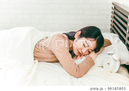 目覚まし時計が鳴っても起きないパジャマ姿の女性（眠い・眠気） 96185803