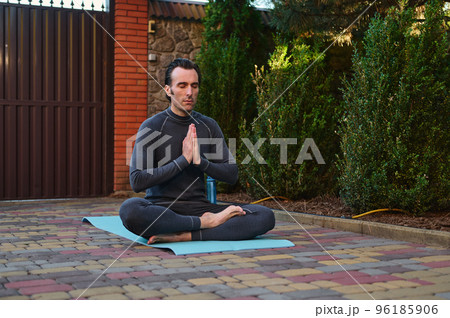 Peaceful Caucasian man athlete, a yogi meditating with his eyes closed in lotus pose, keeping hands palms together, sitting barefoot on a fitness mat. Yoga practice. Spiritual growth. Mindfulness 96185906