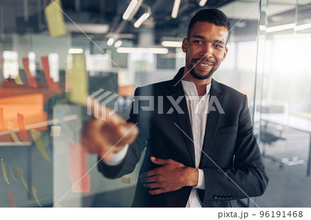 Businessman showing on sticky notes on glass wall while working in modern office 96191468