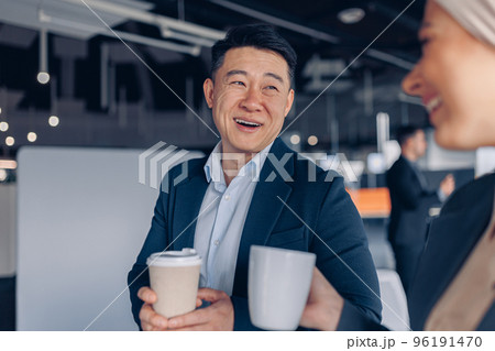 Two happy multiracial colleagues talking and drinking coffee during break time in office 96191470