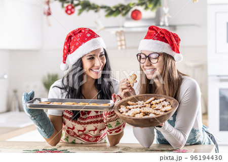 Mother and daughter taste freshly baked Christmas gingerbread Mother and daughter taste freshly baked Christmas gingerbread 96194430