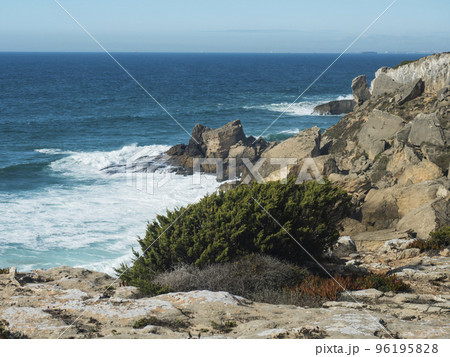 View sea shore with ocean waves, sharp rocks and stones and green bush at Rota Vicentina wild coast near Vila Nova de Milfontes, Portugal. View sea shore with ocean waves, sharp rocks and stones and green bush at Rota Vicentina wild coast near Vila Nova de Milfontes, Portugal. 96195828