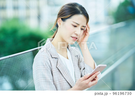 困った表情でスマートフォンの画面を見る若い女性 96196730