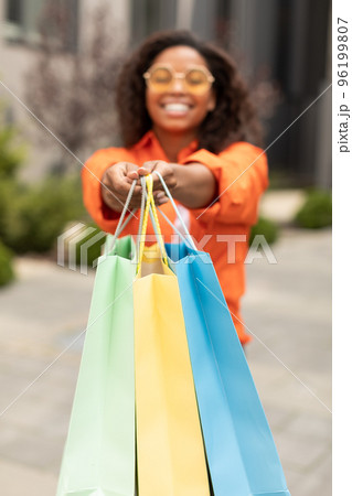 Happy young black woman showing hands with packages with purchases to camera, enjoy sale and shopping Happy young black woman showing hands with packages with purchases to camera, enjoy sale and shopping 96199807
