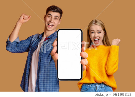 Satisfied emotional young caucasian guy and lady with open mouth enjoy victory, show smartphone with blank screen Satisfied emotional young caucasian guy and lady with open mouth enjoy victory, show smartphone with blank screen 96199812