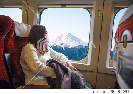 Yong Asian woman wearing mask and holding jacket sitting in the high-speed train while traveling in Japan. 96200091