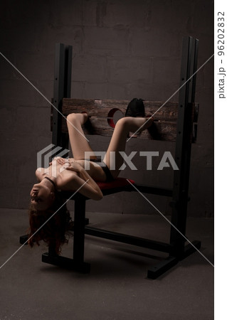 Alluring naked woman lying on BDSM chair 96202832
