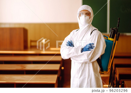 Portrait of man in protective hazmat suit with spray chemicals disinfecting school class. COVID-19. Portrait of man in protective hazmat suit with spray chemicals disinfecting school class. COVID-19. 96203296