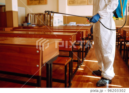 Man wearing protective suit disinfecting school class with spray chemicals to preventing the spread. 96203302