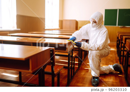 Man in protective hazmat suit washes school desk during coronavirus pandemic. COVID-19. Man in protective hazmat suit washes school desk during coronavirus pandemic. COVID-19. 96203310
