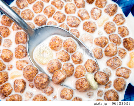 Metal spoon in a plate with milk and corn balls close-up. Metal spoon in a plate with milk and corn balls close-up. 96203635