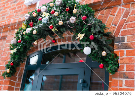 Stylish christmas fir branches with baubles and sparkling garland on front of door at holiday market or restaurant in city street. Winter christmas street decor Stylish christmas fir branches with baubles and sparkling garland on front of door at holiday market or restaurant in city street. Winter christmas street decor 96204076