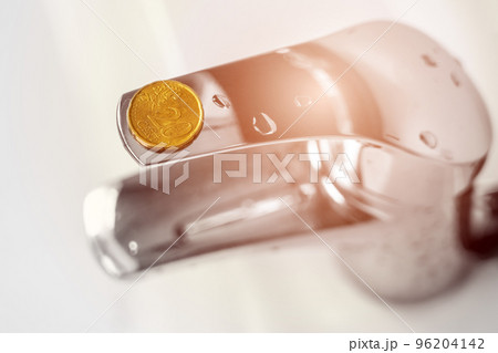 Coin on a bathroom water faucet. Concept of economic crisis and expensive consumption of resources. Idea of saving money in home budget Coin on a bathroom water faucet. Concept of economic crisis and expensive consumption of resources. Idea of saving money in home budget 96204142