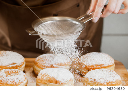 Woman chef prepares fresh donuts in her bakery. Cooking traditional Jewish Hanukkah Sufganiyot. Small business concept. Woman chef prepares fresh donuts in her bakery. Cooking traditional Jewish Hanukkah Sufganiyot. Small business concept. 96204680