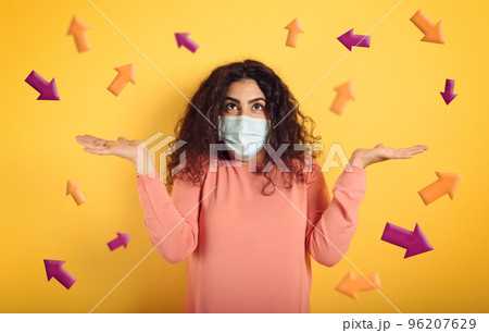 Girl with face mask is confused which arrow to follow. Concept of doubt about laws governing covid-19. Yellow background 96207629