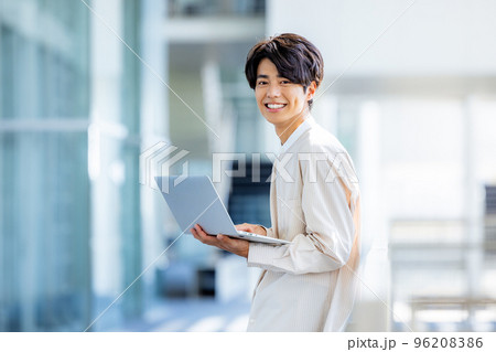 オフィスのロビーでノートパソコンを持って立っている若い男性 96208386