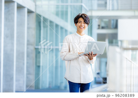 オフィスのロビーでノートパソコンを持って立っている若い男性 96208389