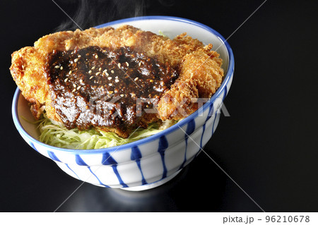 キャベツもたっぷり敷かれている熱々味噌カツ丼を黒背景で撮影 96210678